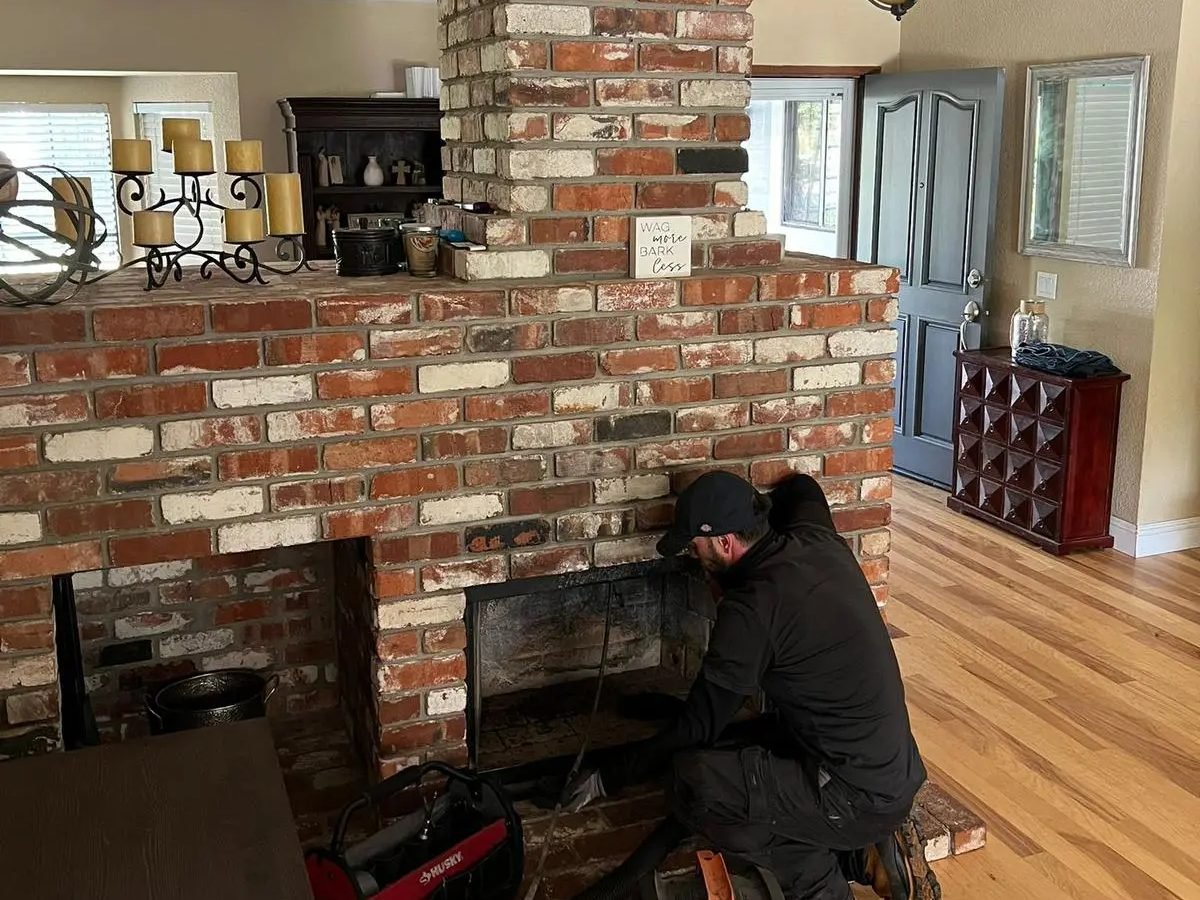 Advanced Chimney Sweep Solutions technician sweeping a floor-to-ceiling brick fireplace with the vacuum running