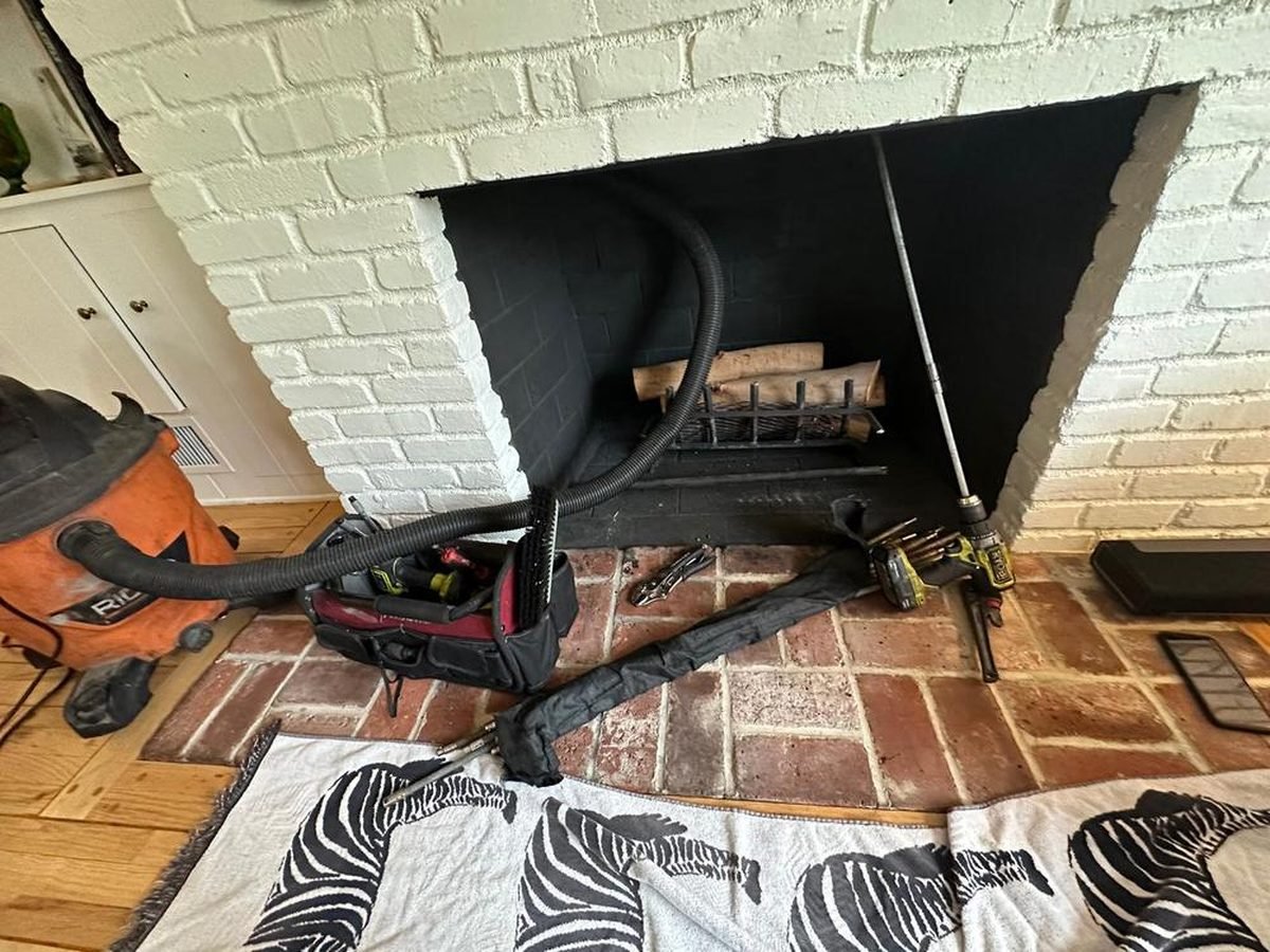 HEPA vacuum hose, rods and drop sheets set up at a sealed white brick firebox during a chimney sweep