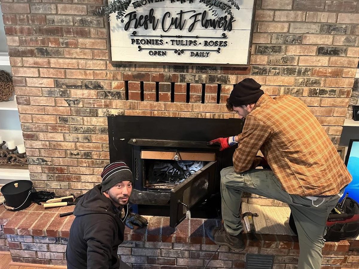Two technicians working on the damper and firebox of a brick fireplace during a repair visit