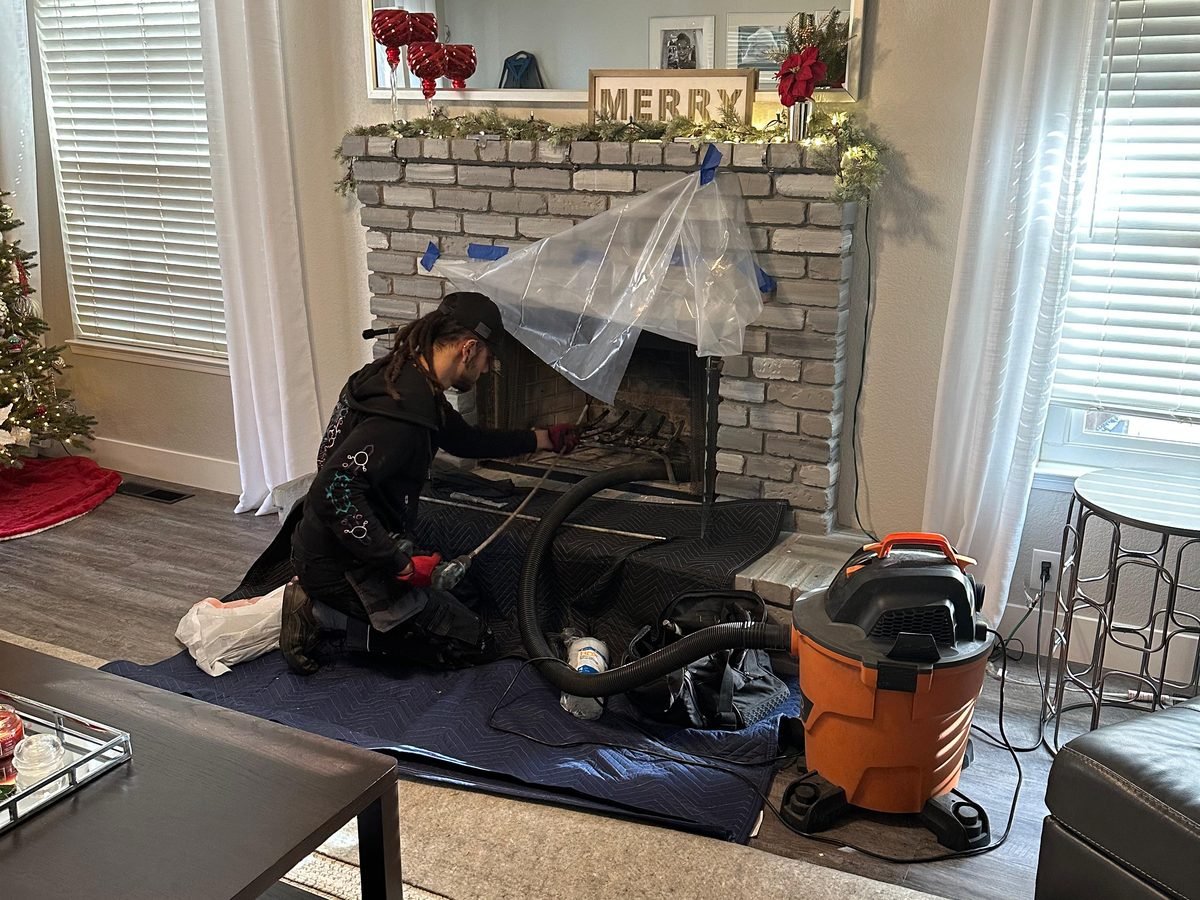 Technician sealing a fireplace opening with sheeting before sweeping, floor covered throughout the room