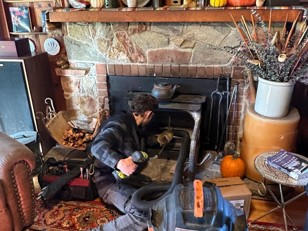 Technician inspecting a wood stove insert set into a stone fireplace during a service call