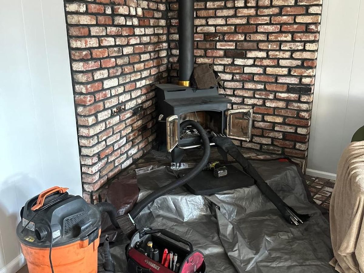 Wood stove in a brick alcove protected with tarps during a connector pipe and flue cleaning
